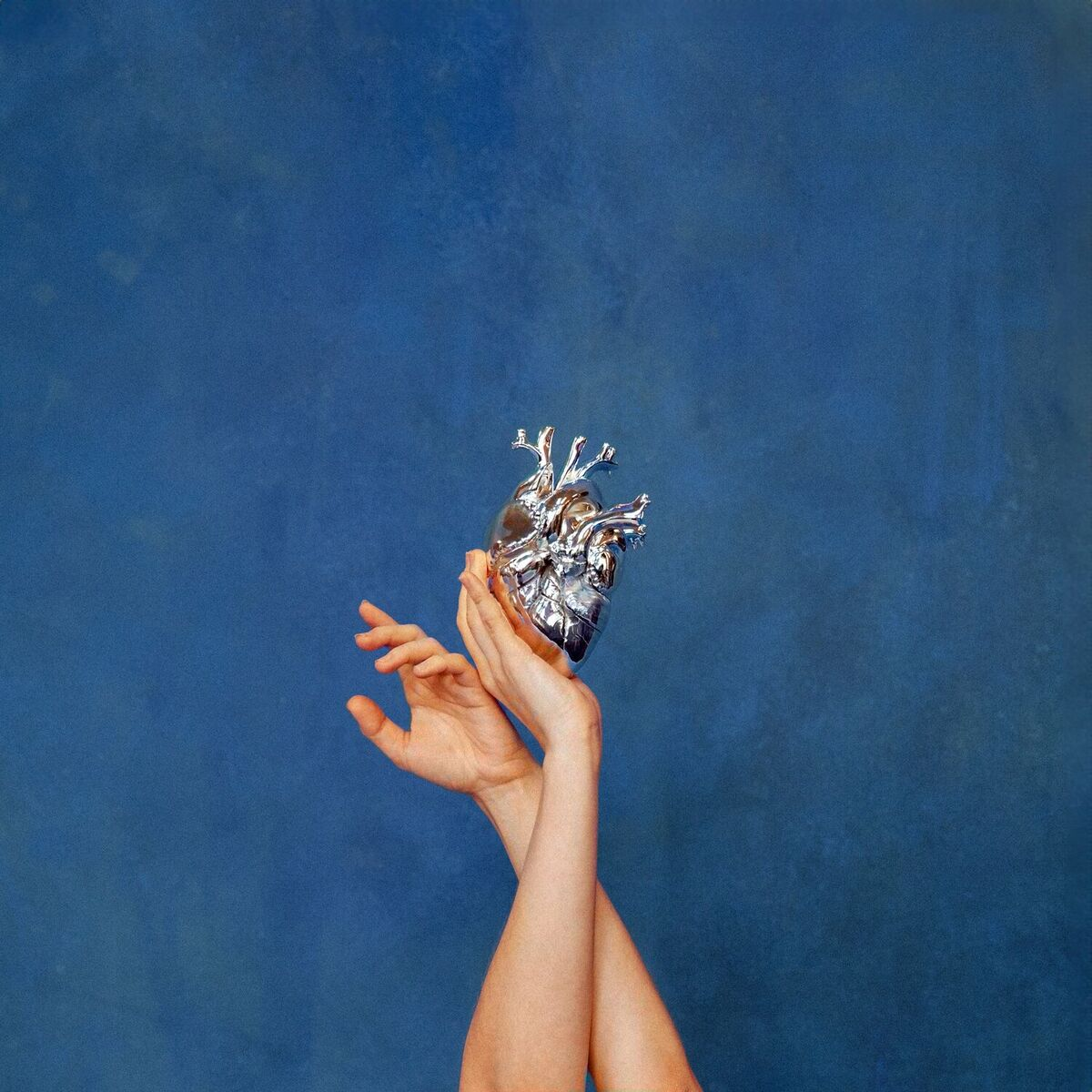 Cover of What Happened to the Heart by Aurora. A blue background, with two hands holding a metal human heart.