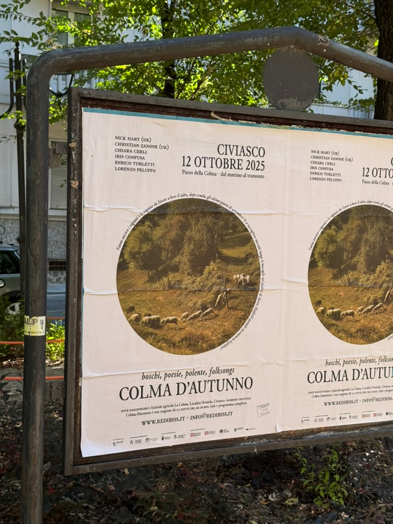 Event poster for "Colma d'Autunno" dated October 12, 2025, featuring circular image of pastoral scene with sheep, mounted on outdoor bulletin board.